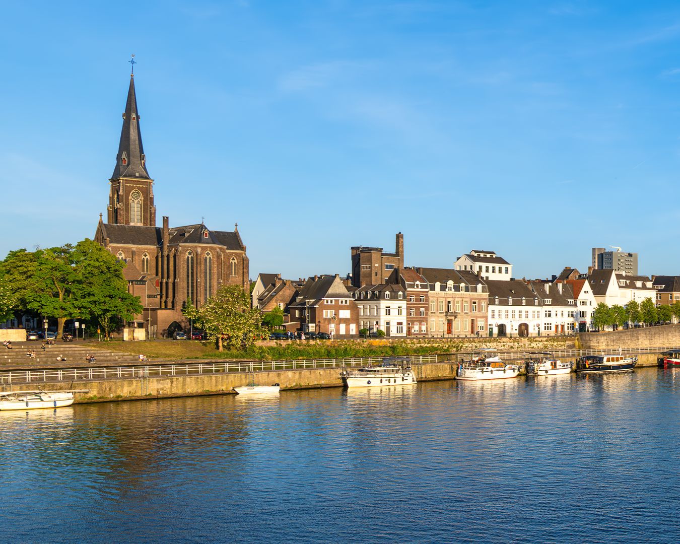 Casas históricas e igreja à beira do Rio Mosa com barcos atracados na cidade de Maastricht