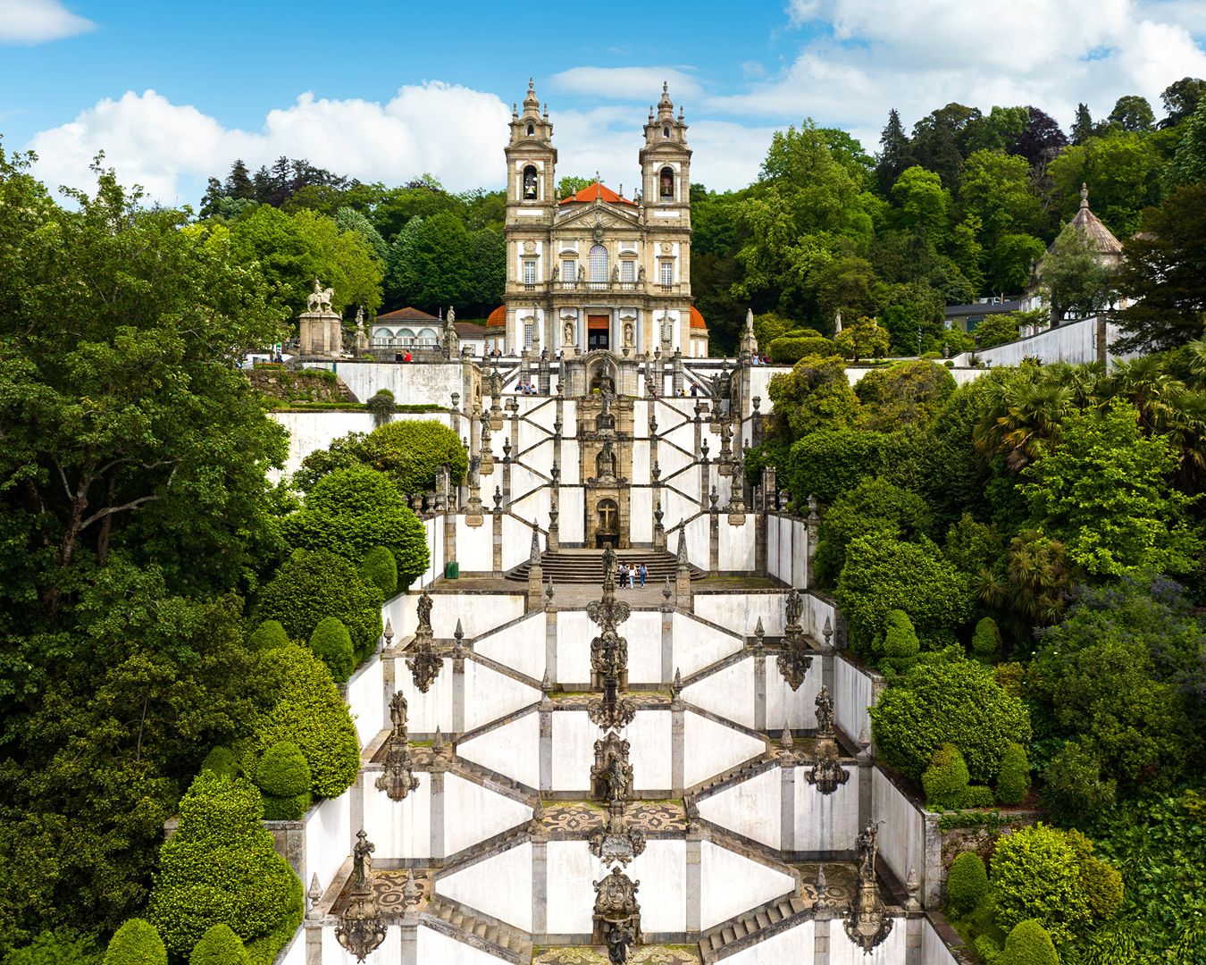 Escadaria barroca em ziguezague do Santuário do Bom Jesus do Monte cercada por vegetação em Braga, Portugal.