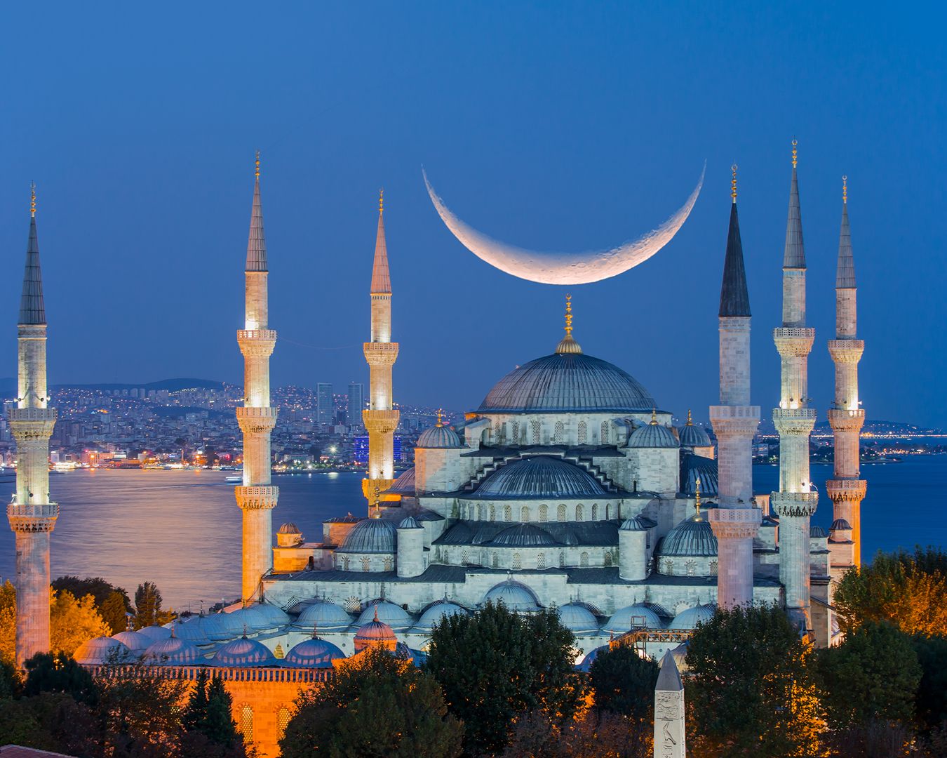 Vista noturna iluminada da Mesquita Azul com os seus seis minaretes e uma lua crescente ao fundo em Istambul, Turquia.