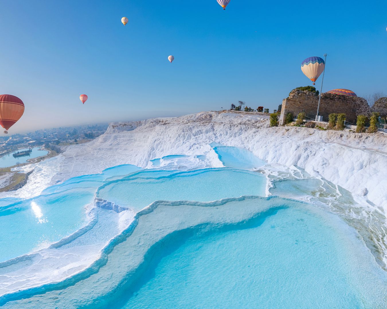 Terraços de travertino branco e piscinas termais turquesa de Pamukkale com balões de ar quente no céu, Turquia.