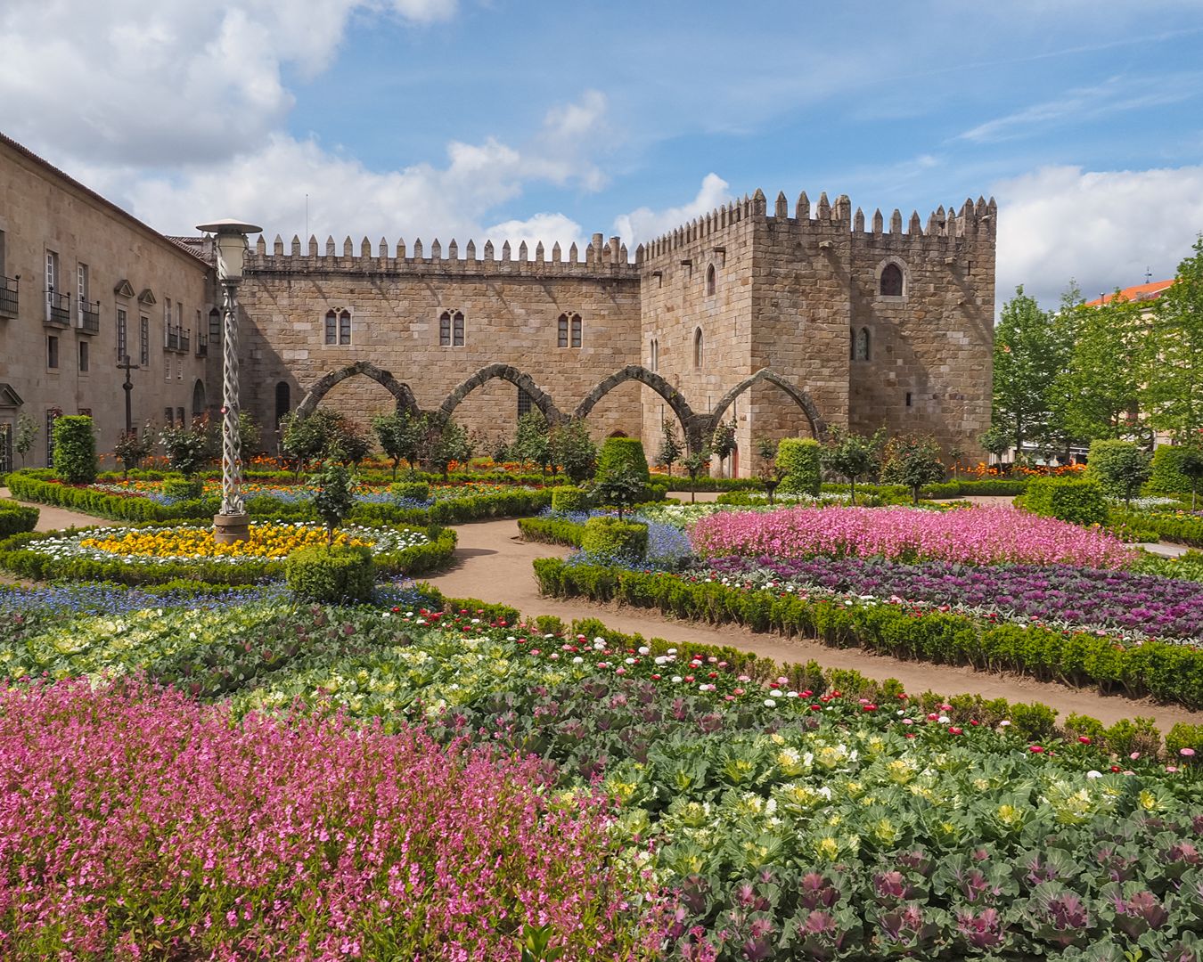 Jardim de Santa Bárbara florido em Braga com o Paço Episcopal e arcadas medievais de pedra ao fundo.