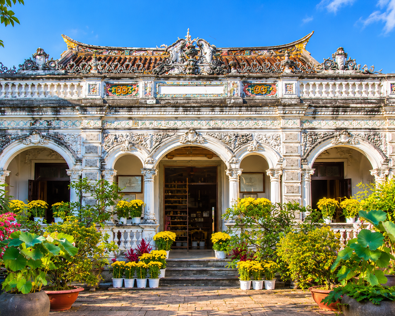 Fachada da histórica casa colonial Binh Thuy em Can Tho, Vietnã, cercada por vasos de flores amarelas