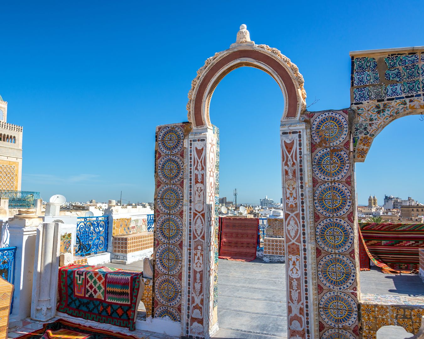 Terraço decorado com arcos de azulejos e tapetes orientais com vista para o minarete da mesquita na Medina de Túnis