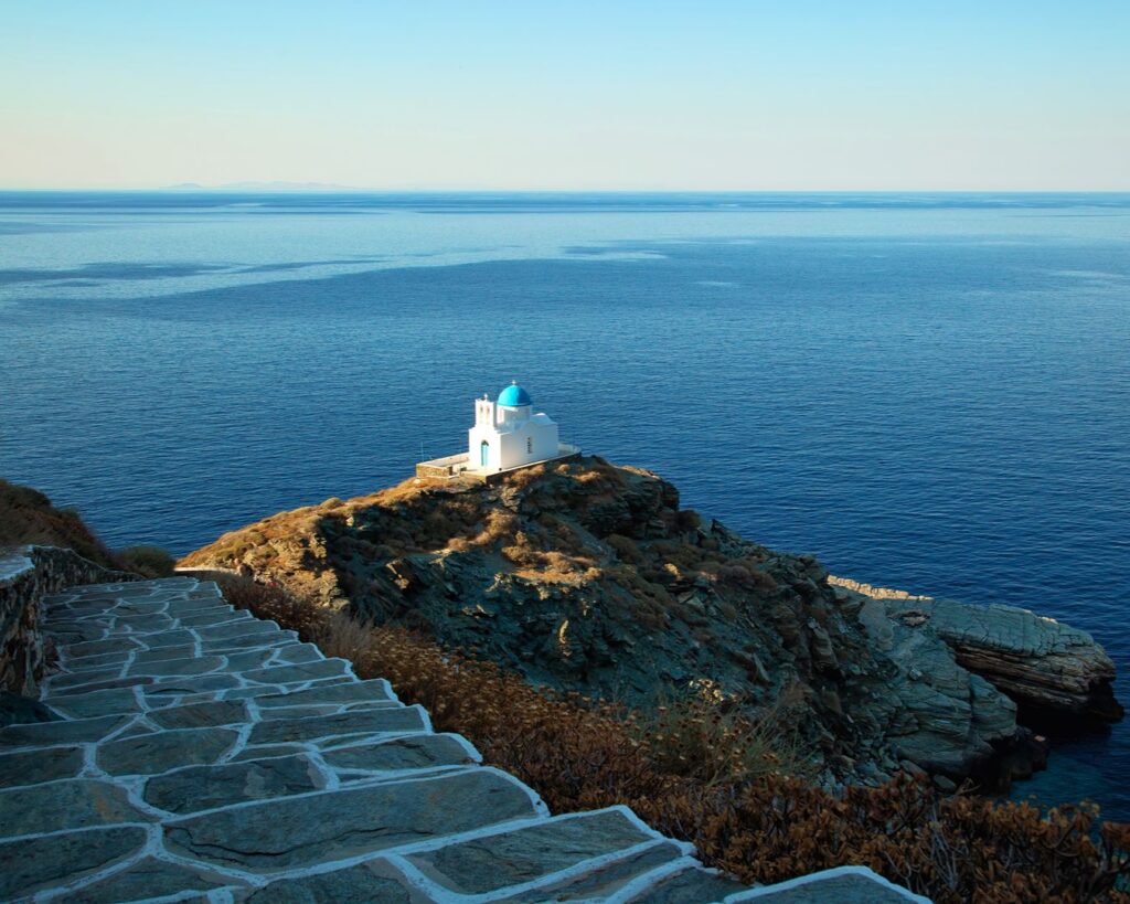 Igreja das Sete Dores com cúpula azul no topo de penhasco com vista para o mar em Sifnos, Grécia