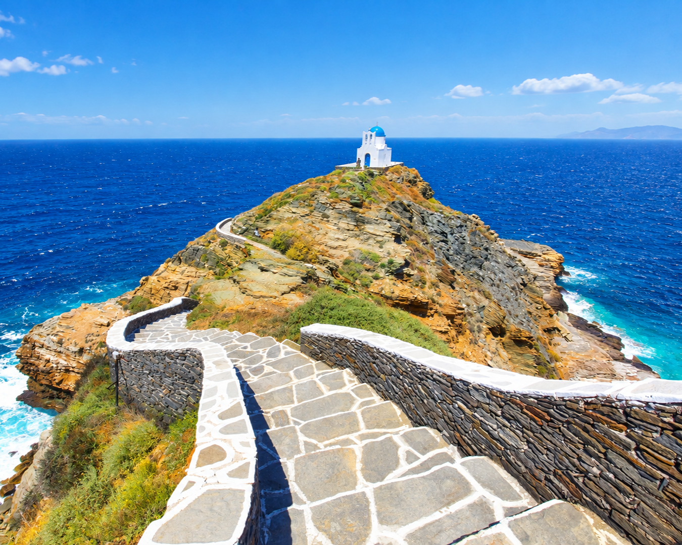 Escadaria de pedra contornando a penhasco em direção a uma capela branca com cúpula azul sobre o mar