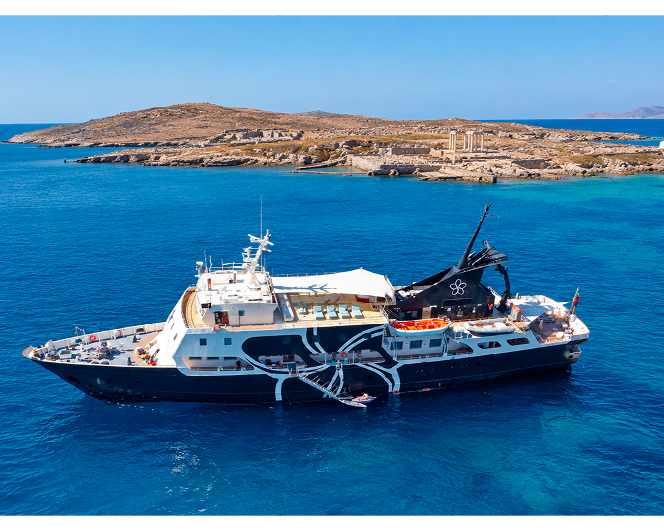 Navio de cruzeiro e iate de luxo preto navegando no mar azul turquesa próximo à costa de uma ilha grega