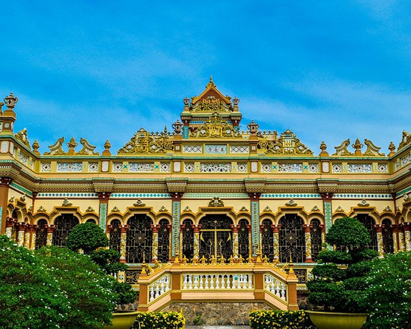 Fachada ornamentada do pagode Vinh Trang com detalhes dourados e plantas no jardim em My Tho, Vietnã